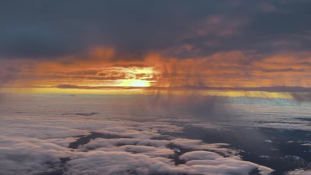 An arrial view of a burning sunrise over The Alps range captured from a jet cockpit flying at cruise between layers of clouds with a rising sun in the horizon.