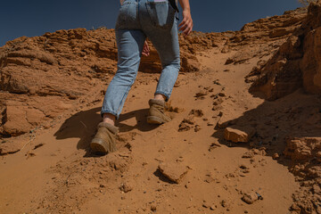 A female hiker ascends a clay slope in Mongolia's "Grand Canyon" near the Sphinx rock. Rear-side view captures her boots and sole imprints on the desert ground in medium shot.