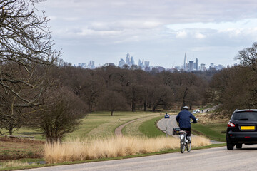 Cyclist and car sharing the road in a London park with the city skyline beyond