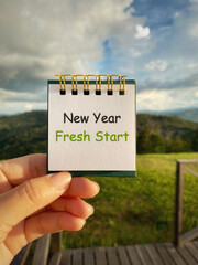 Note with “New Year Fresh Start” held outdoors, representing new beginnings, renewal, and goal...