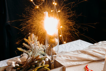 Sparkler burning on festive table with candle and greenery. Bright holiday celebration moment and magical winter atmosphere.