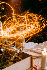 Long exposure light trails above glass with candle and festive decor. Magical holiday atmosphere and creative Christmas celebration concept.