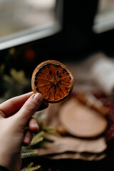 Hand holding dried orange slice in warm winter light. Cozy Christmas preparation mood and natural festive detail.