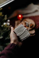 Hands holding a white spool of twine for gift wrapping near warm Christmas lights. Cozy holiday crafting moment and rustic festive decoration concept.