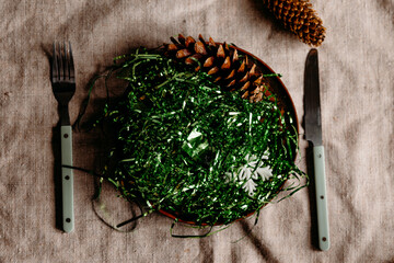Creative Christmas tree made from green tinsel on linen background with cutlery. Playful festive flat lay concept.