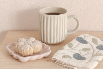 Horizontal shot of minimal table with coffee cup, pastry, and casually folded folk-embroidered napkin, modern Scandinavian-style interior, warm soft daylight, shallow focus on embroidery texture.