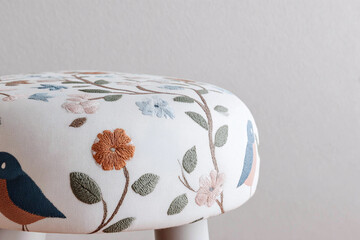 Top-down horizontal shot of upholstered seat fabric with modern folk motifs, dark base textile, delicate stitched birds and florals, soft daylight, minimal styling, clean composition.