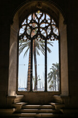 View through ancient gothic cathedral window on palm trees and yacht marina