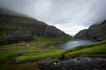 A narrow valley opens toward water under a low ceiling of cloud. The church rests within the land rather than apart from it, shaped by terrain and weather more than intention.