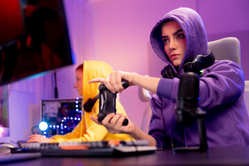 young woman in a purple hoodie working or gaming at a computer in a modern, neon-lit room, digital lifestyle, remote work, live streaming, or esports. Gamer controlling joystick for video game.