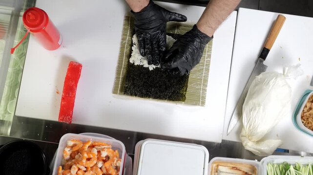 Sushi master spreads rice on nori in close-up. The process of making sushi in a Japanese restaurant. The chef's hands are gloved. Top view. 