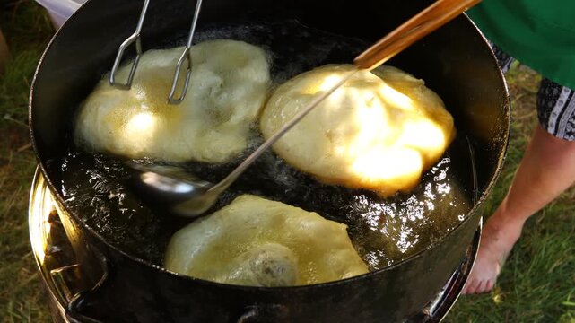 Traditionally way of cooking, frying dough in oil or pork fats making delicious treat in a large rustic pot, deep iron cauldron over open fire.