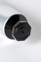 Close-up of a silver aluminum cosmetic tube end with black cap on a white background.