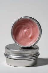 Pink cosmetic balm texture in silver tin on white background.