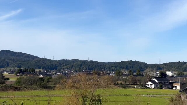 Moving car footage along a countryside highway in mountain Japan captures scattered houses and farm plots below green ridges, as the ride advances through wide calm scenery