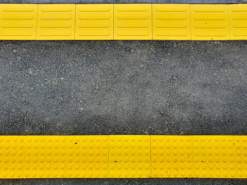Yellow tactile paving safety warning lines on a dark asphalt train station platform.