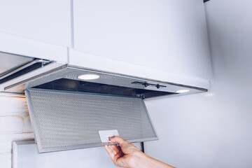 A Hand Reaches for a Modern Kitchen Ventilation Filter Drawer with Bright LED Lights Below, Showcasing a Clean and Functional Design Element.