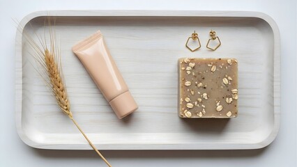 Flatlay of skincare product tube, oat soap, gold earrings and wheat on a white tray for beauty blog
