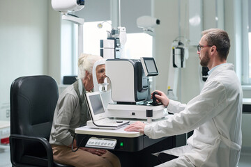Senior Caucasian woman undergoing eye examination with ophthalmologist using advanced diagnostic...