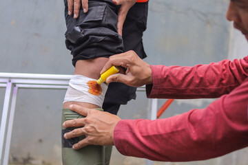 Construction Worker in Pain Holding Knee While Colleague Administers First Aid