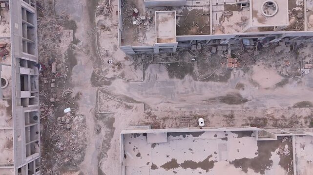 Drone view of a huge unfinished shopping mall or office complex. Features stagnant green water pools, rusted rebar, and overgrown pathways, depicting total economic failure and urban decay.