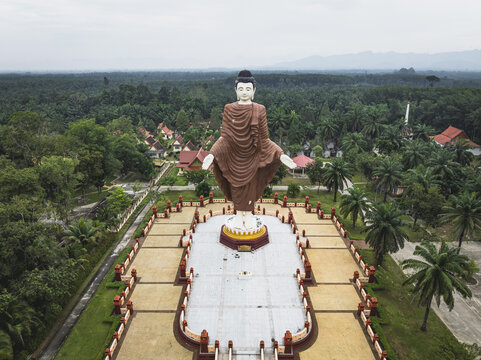 Aerial view of a towering Buddha statue standing majestically against a backdrop of lush green trees, creating a striking contrast, Tambon Pratuchai, Chang Wat Phra Nakhon Si Ayutthaya, Thailand.