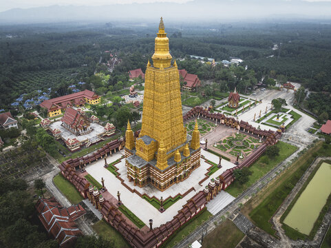 Aerial view of the majestic golden Wat Bang Thong temple rises amidst lush greenery, its intricate architecture gleaming under the soft light, Tambon Pratuchai, Thailand.
