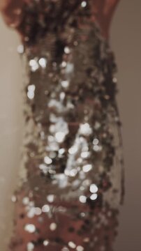 Blurred view of dancing woman wearing sparkling silver sequin dress, holding a cocktail in a crystal glass. Festive glamorous evening mood. Christmas celebration