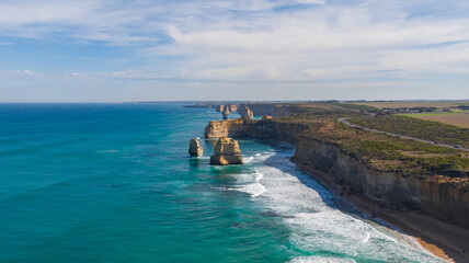 Aerial view of majestic limestone stacks meet the turquoise ocean under a vast sky along the Twelve Apostles coastline, Twelve Apostles, Victoria, Australia.