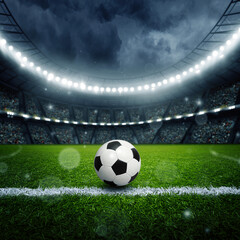 Dramatic clouds gather over a soccer field at night with bright lights shining and a ball resting on the grass