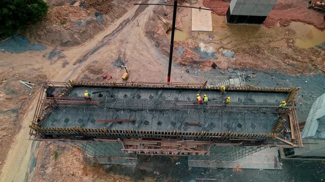 Aerial view of construction workers installing steel reinforcement and preparing the bridge deck at a highway construction site. Large-scale reinforced concrete bridge and infrastructure project.