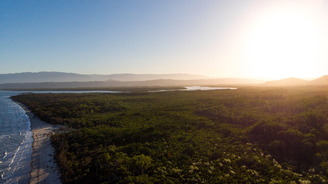 Aerial view of the sun kissing the lush green canopy as waves gently caress the sandy shore, Cape Tribulation, Queensland, Australia.