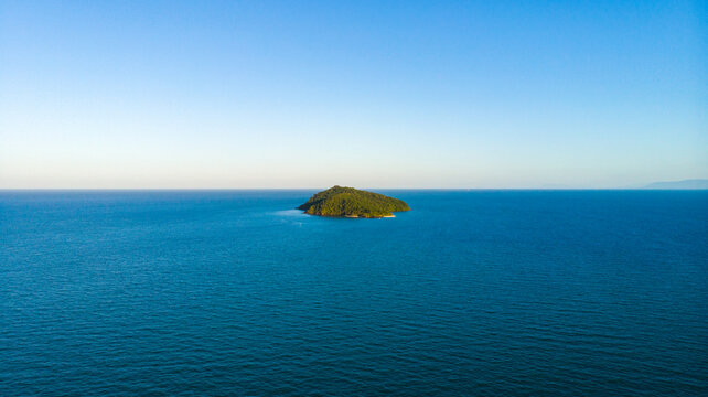 Aerial view of a verdant island rises amidst the vast expanse of the turquoise sea, a jewel in the ocean's embrace, Cape Tribulation, Queensland, Australia.