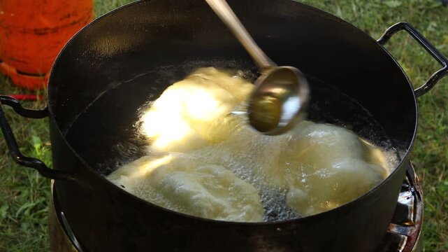 Traditionally way of cooking, frying dough in oil or pork fats making delicious treat in a large rustic pot, deep iron cauldron over open fire.