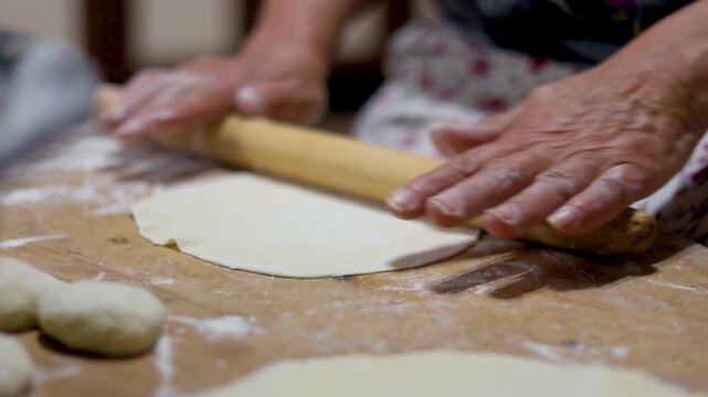 Close-up of an elderly woman's female hands rolling out dough with a wooden rolling pin. Making homemade pies and chebureks.