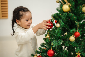 toddler girl decorating toy ball on Christmas tree at home