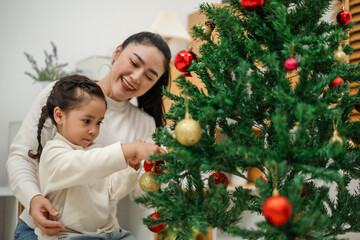 mother and toddler girl decorating Christmas tree with toy ball at home