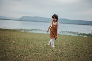 happy toddle girl walking on grass field near the river