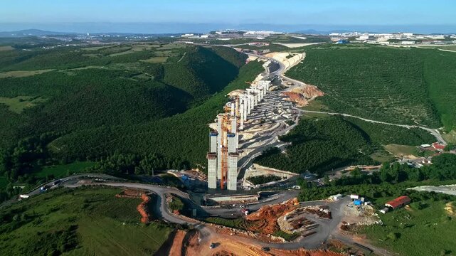 Drone aerial view of a long highway viaduct under construction with multiple reinforced concrete bridge piers extending through a green valley. Large-scale infrastructure and transportation developmen