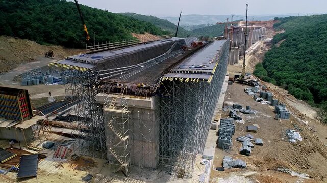 Drone view of a large viaduct deck under construction with extensive scaffolding and formwork at a highway construction site. Civil engineering and infrastructure development in mountainous terrain.