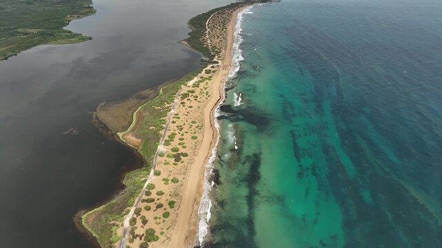 Aerial view of the dark lagoon contrasting with the turquoise sea, divided by a narrow strip of sandy beach and sparse vegetation, Korission, Corfu, Greece.