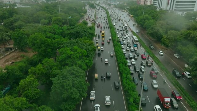 Aerial view of traffic congestion on National Highway 48, with vehicles snaking between green trees and modern buildings, Gurugram, Haryana, India.