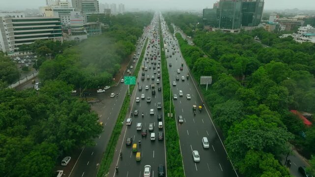 Aerial view of traffic flowing along National Highway 48, flanked by dense green trees, with buildings in the background, Gurugram, Haryana, India.