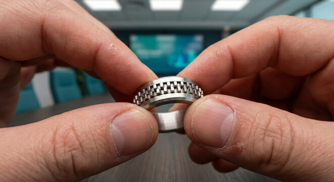 Close up of hands playing with metal fidget ring during office meeting for stress relief.