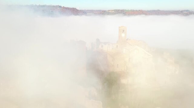 Aerial view of Celleno's ancient buildings, shrouded in ethereal fog, creating a dreamy, almost surreal landscape, Celleno, Lazio, Italy.