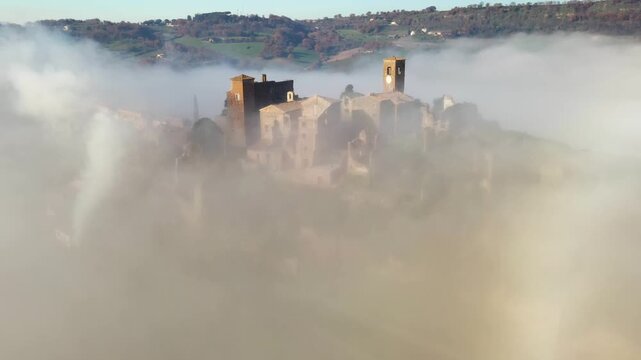 Aerial view of Celleno's ancient buildings shrouded in thick, ethereal fog, creating a dreamlike landscape of muted tones and softened edges, Celleno, Lazio, Italy.
