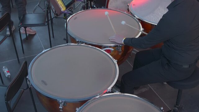 Close View Of Timpani Player Adjusting Pitch Amidst Orchestral Rehearsal With Dramatic Lighting. Media
