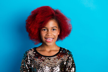 Happy young girl with red dyed hair wearing a sequined top against a bright blue background