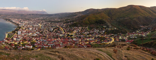 Aerial panorama of Pogradec, Albania, showing illuminated streets, residential districts, and surrounding hills during twilight.