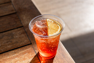 A refreshing drink in a clear plastic cup filled with sparkling orange soda. The cup is placed on a wooden table with a blurred background.